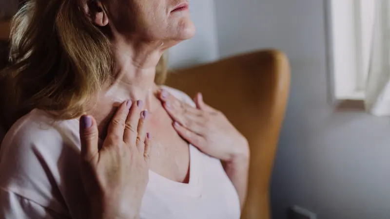 Une femme porte les mains à la base de son cou.